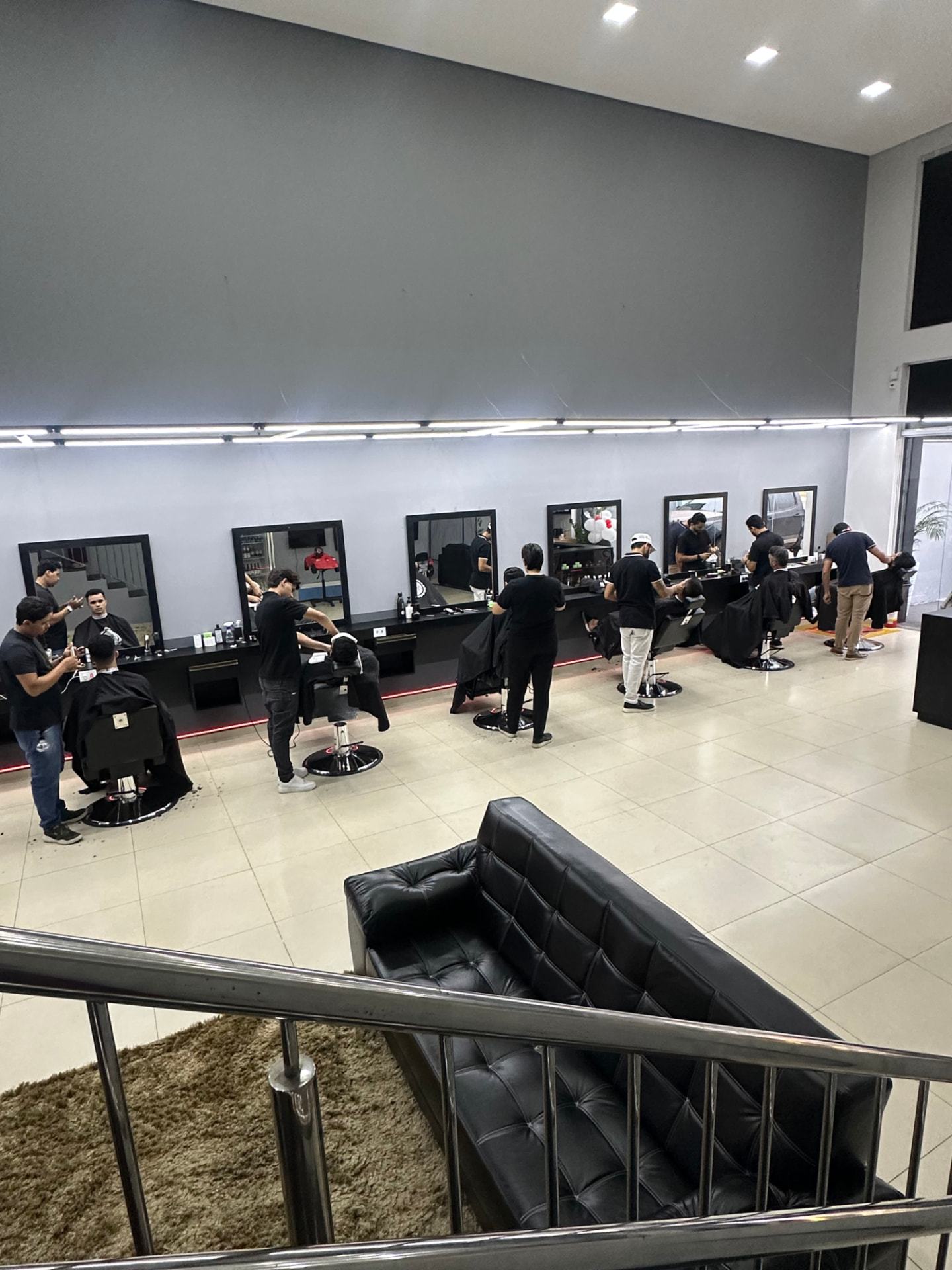 Interior da AUX Barbearia com estações de trabalho e barbeiros atendendo